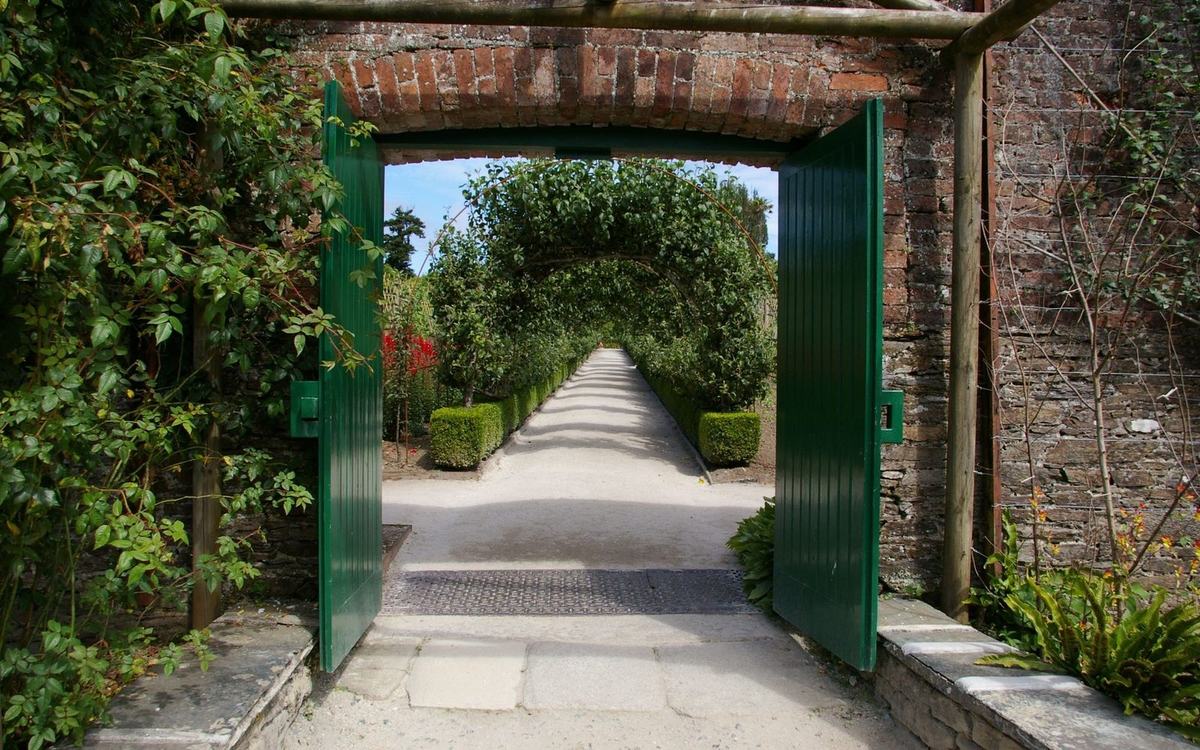 Open green painted timber gate in a brick garden wall